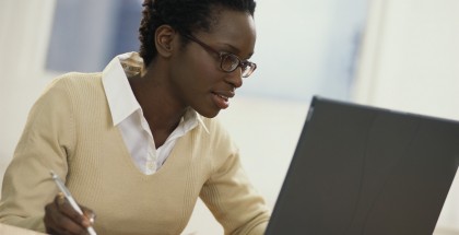 Young Woman with Newspaper Using Laptop